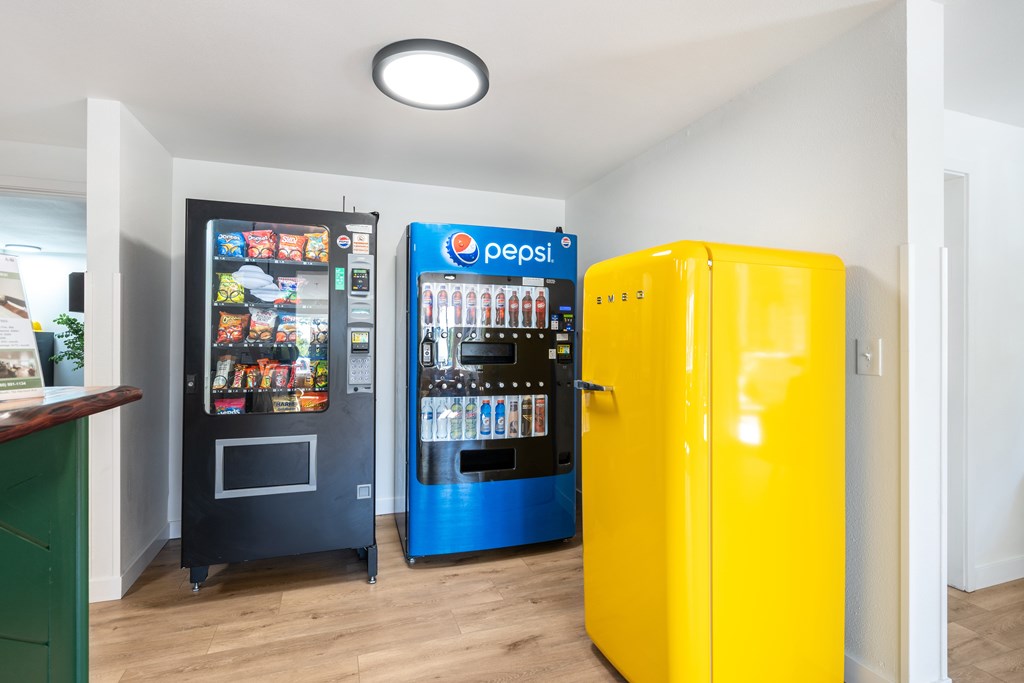 A yellow fridge is in front of a Pepsi machine.