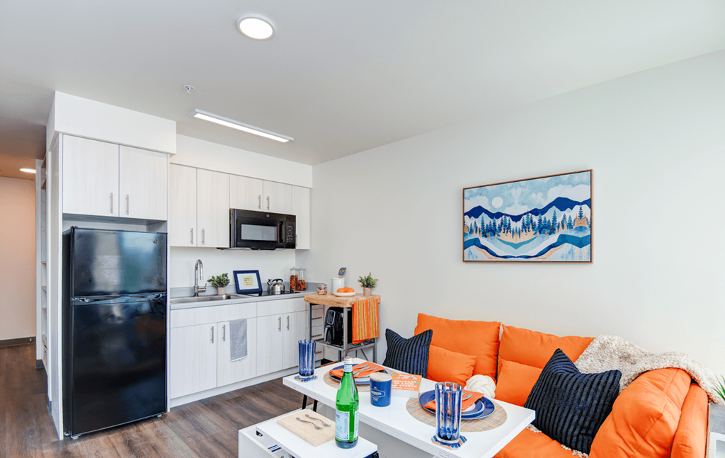 a living room with an orange couch and a kitchen with a black refrigerator