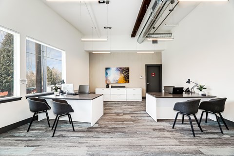 A modern office space with a large desk, chairs, and a view of trees outside the window.