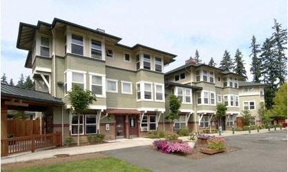 A large, modern building with a green and beige exterior and a parking lot in front.