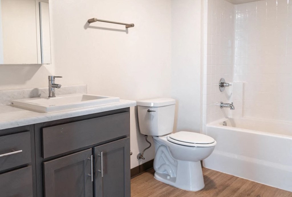A white toilet sits in a bathroom next to a sink and bathtub.