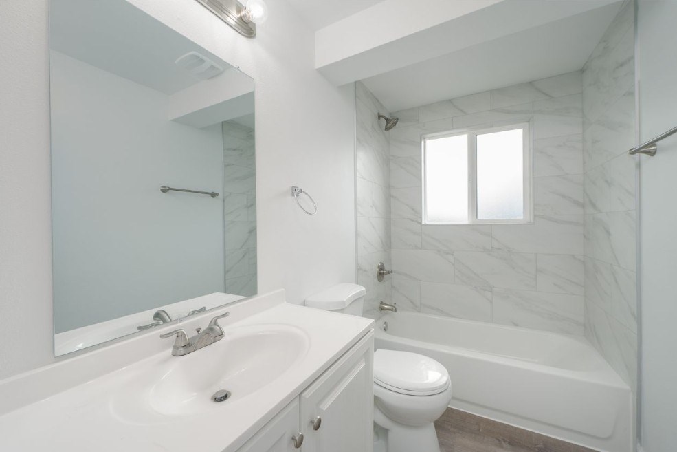 A white bathroom with a marble wall and a window.