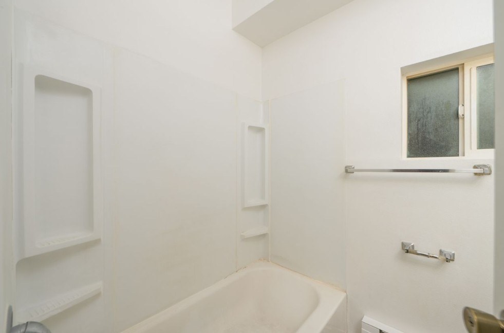 A white bathroom with a tub and a window.
