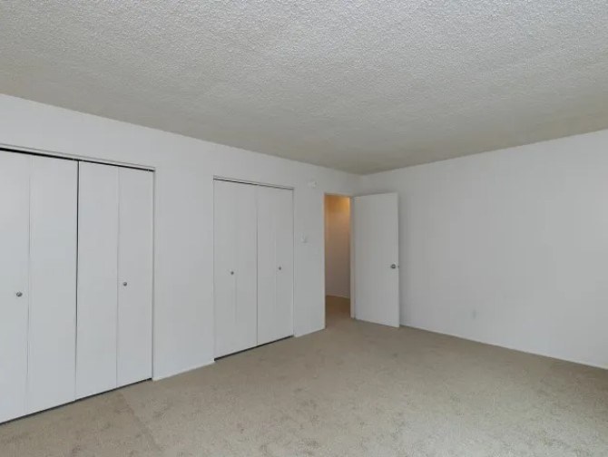 A room with white walls and a carpeted floor with three doors.