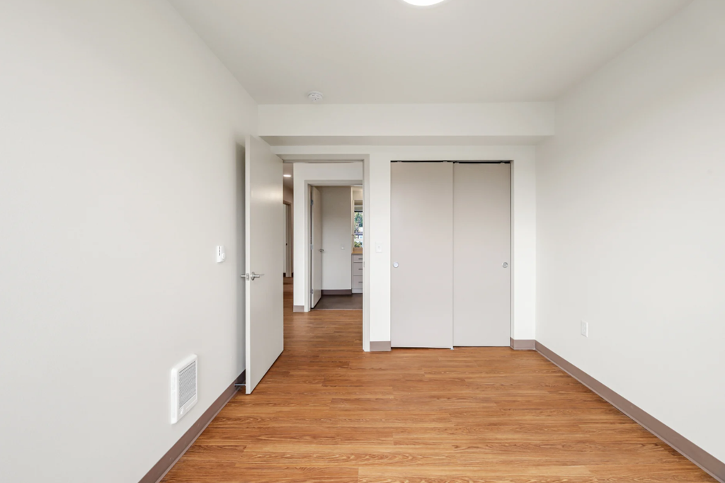 a hallway with white walls and wood floors and a closet