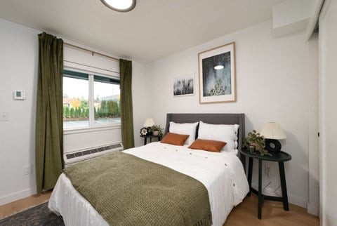 A bedroom with a large bed and a window with green curtains.