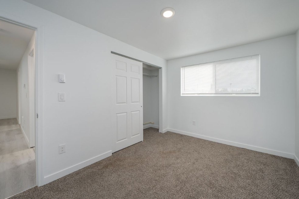 A room with a carpeted floor and a window with blinds.
