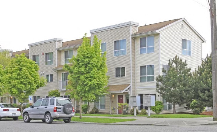 A grey car is parked in front of a two-story apartment building.