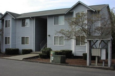 A grey two story apartment building with a mailbox in front.