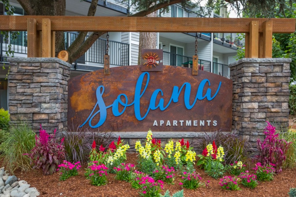 A sign for Solana Apartments is surrounded by flowers.