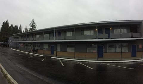 A grey building with a parking lot in front of it.