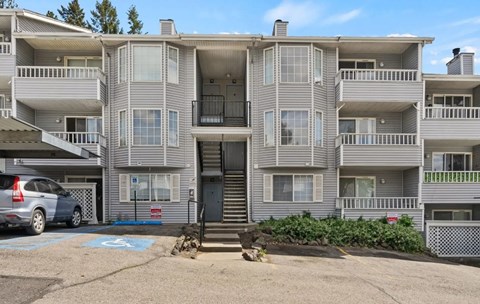 A grey apartment building with a car parked in front.
