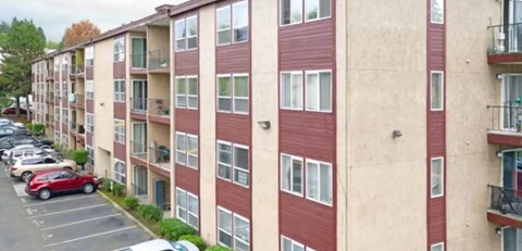 A red car is parked in a parking lot in front of apartment buildings.