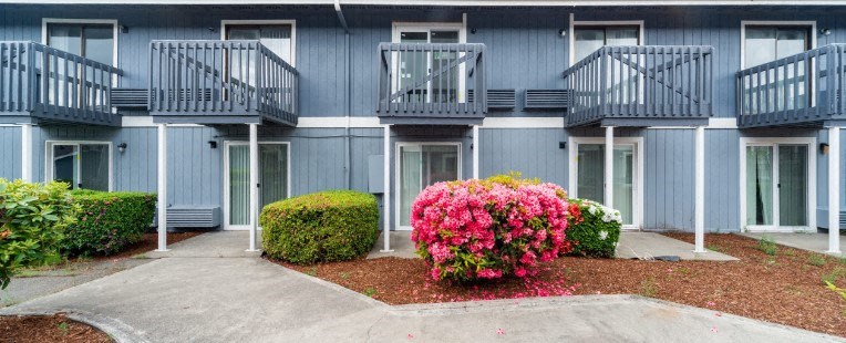 an apartment building with blue exterior and pink flowers in front