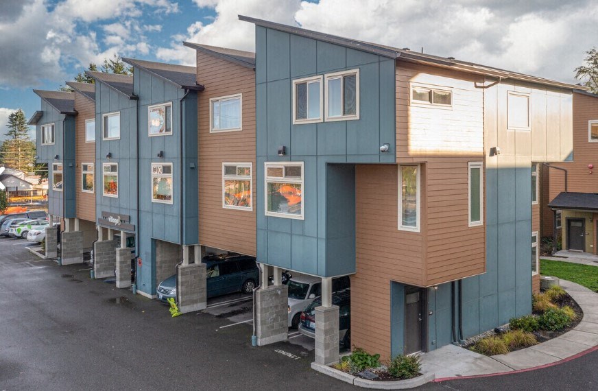 A row of modern townhouses with a parking lot in front.