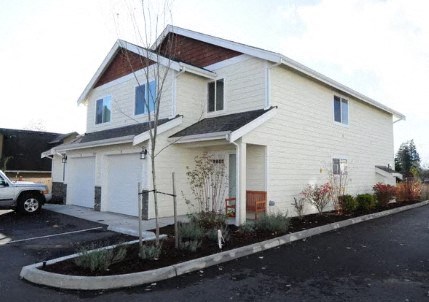 A white house with a brown roof and a grey car parked in front.