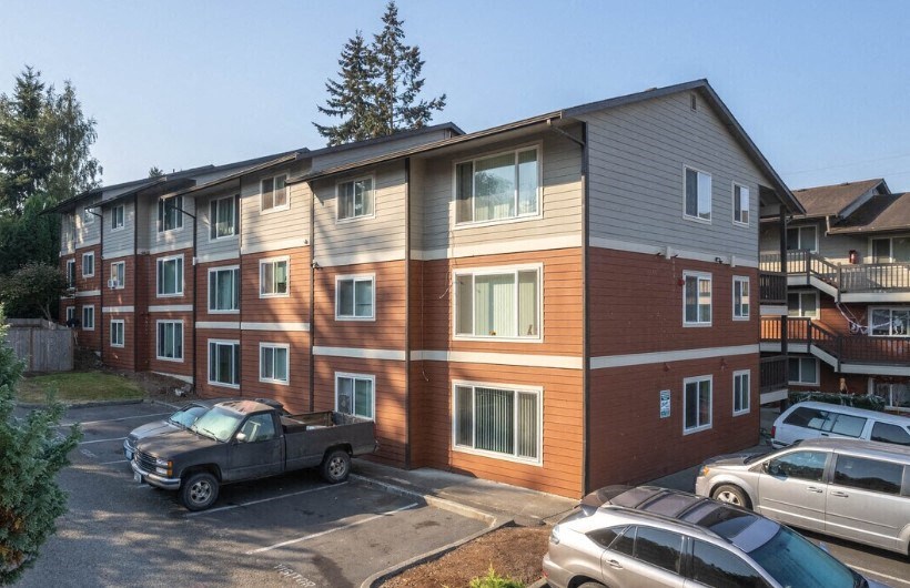A grey pickup truck is parked in a parking lot in front of a two-story apartment building.