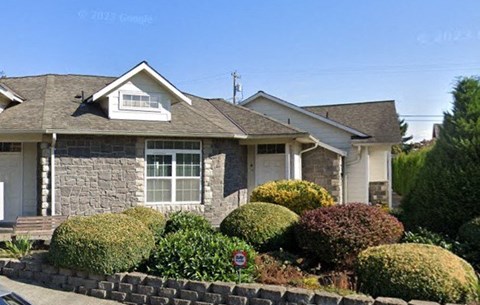 A house with a grey roof and a white door is surrounded by a well-manicured garden.