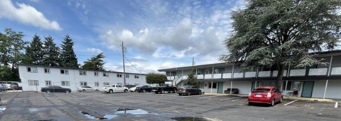 A parking lot with a white building and a red car.