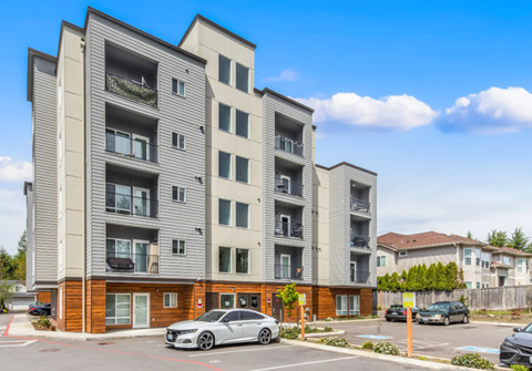A modern apartment building with a grey car parked in front.