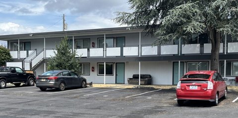 A red car is parked in a parking lot in front of a building with a tree.