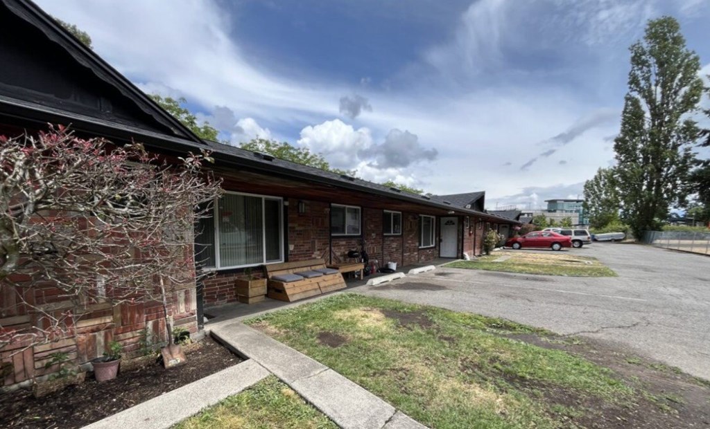 A red car is parked in the driveway of a brick house.