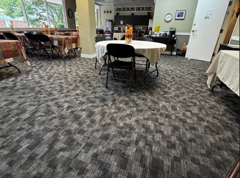 A room with a carpeted floor and tables with chairs.