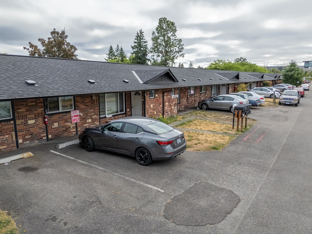 A grey car is parked in a parking lot in front of a brick building.