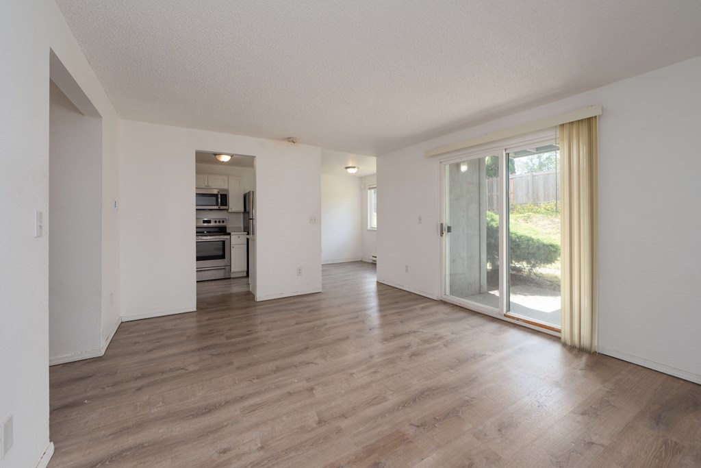A spacious room with wooden flooring and a sliding glass door leading to a garden.