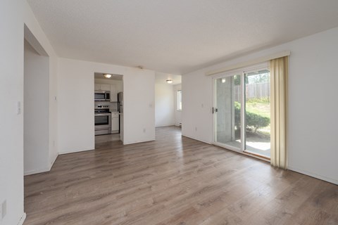 A spacious room with wooden flooring and a sliding glass door leading to a garden.