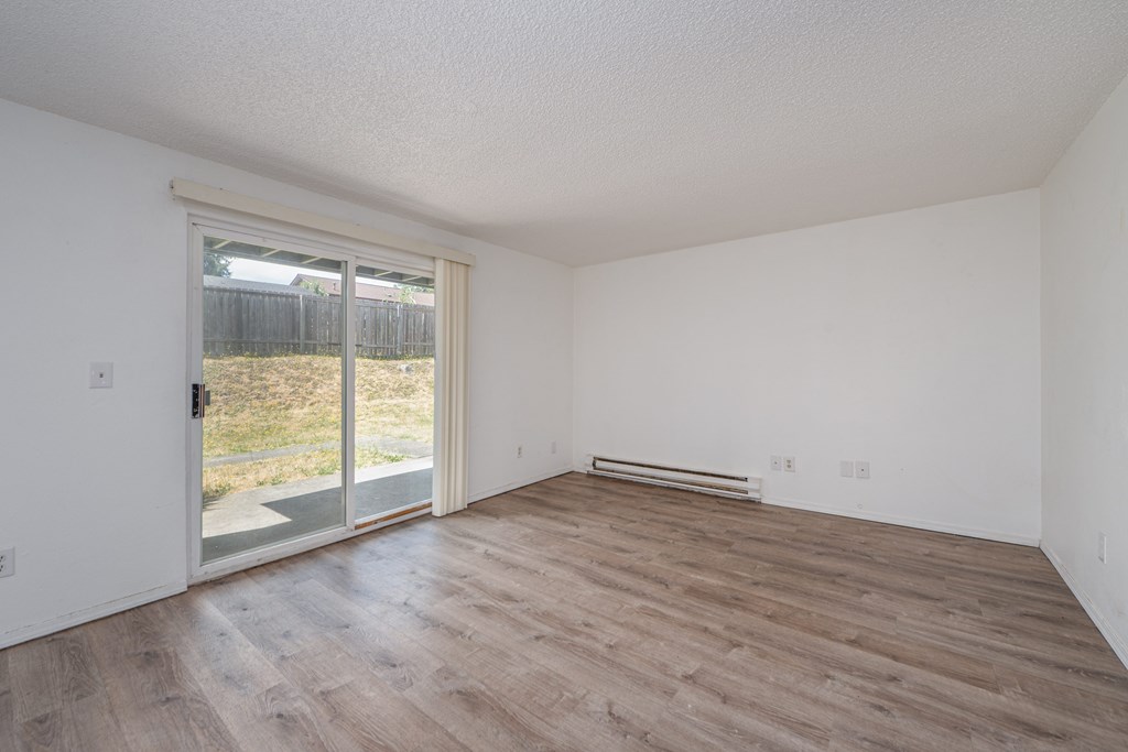 Empty room with wooden flooring and sliding glass doors.
