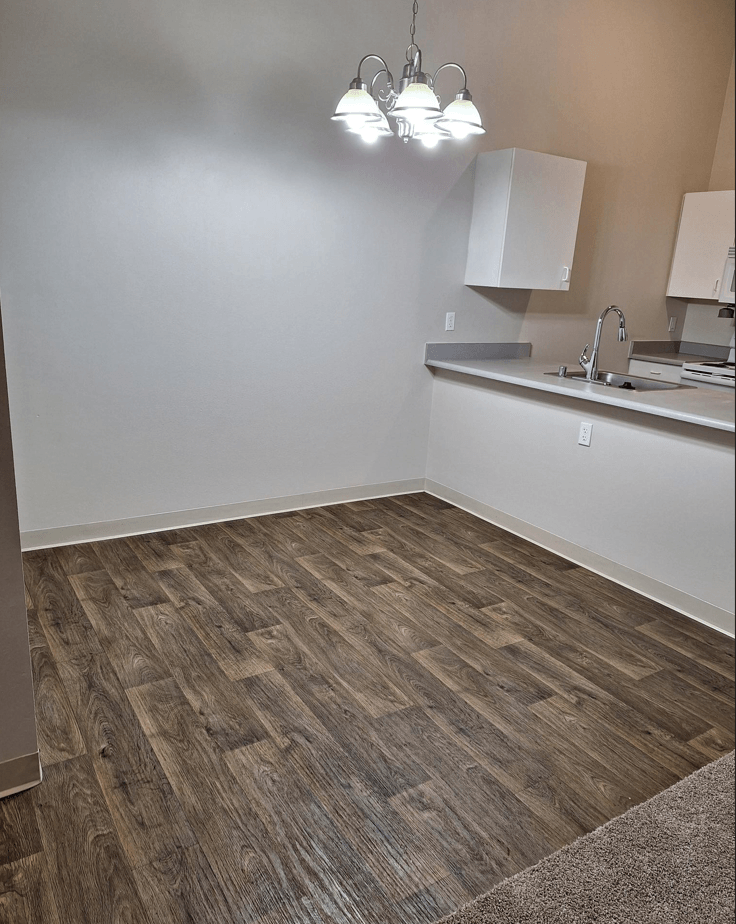 an empty living room with wood flooring and a kitchen