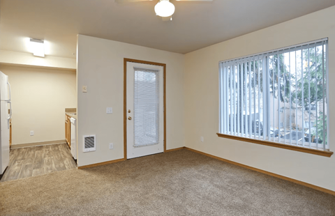 A room with a carpeted floor, a window with blinds, and a door leading to another room.