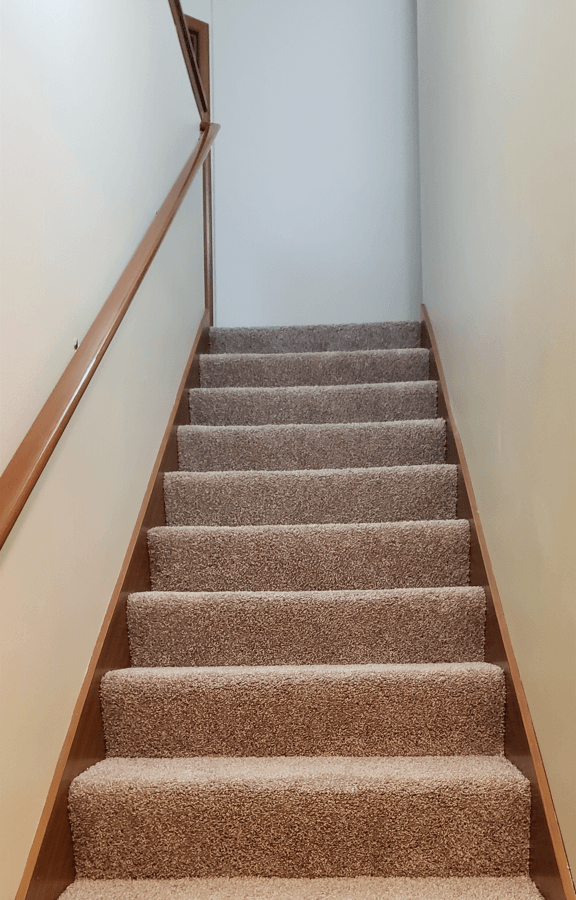 a set of carpeted stairs with a white wall and brown railing
