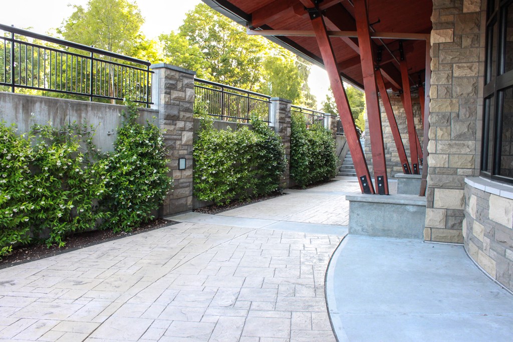 a walkway leading to a building with stone walls and hedges