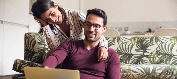 a man and woman sitting on a couch looking at a laptop