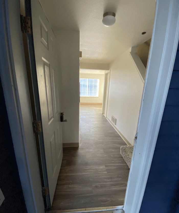 a view down a hallway with a white door and wood flooring