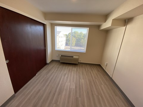 A room with a brown door and a window showing a view of a building and trees.