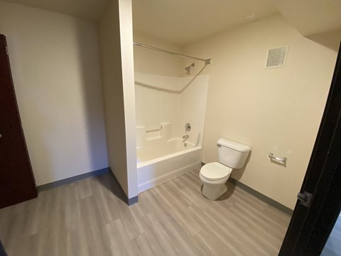 A white toilet sits in a bathroom with a white tub and a white shower head.
