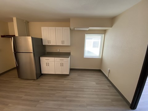 A kitchen with a refrigerator, cabinets, and a window.