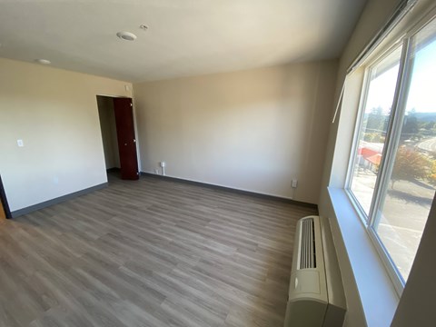 A room with a wood floor and a window overlooking a parking lot.