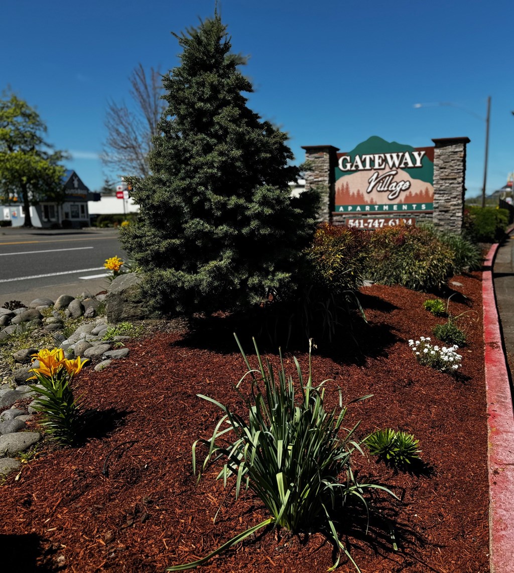 A sign for Gateway Village Apartments is in front of a tree.