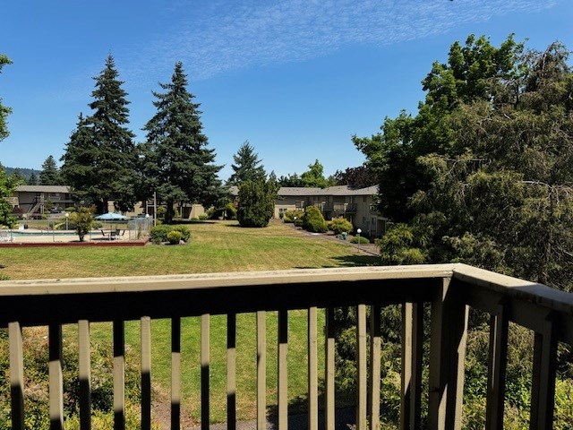 A wooden deck overlooks a grassy area with trees and a building in the distance.