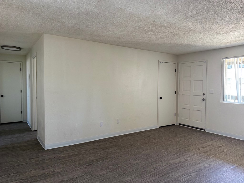 A room with white walls and wood flooring, with two doors and a window.