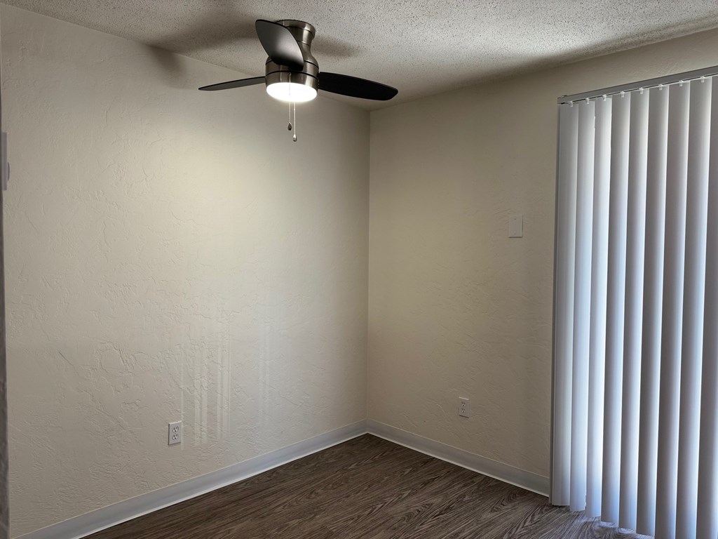 A room with a ceiling fan and a window with blinds.