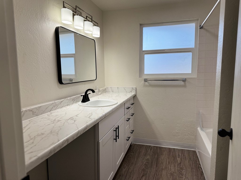 A bathroom with a marble countertop and a mirror with lights above it.