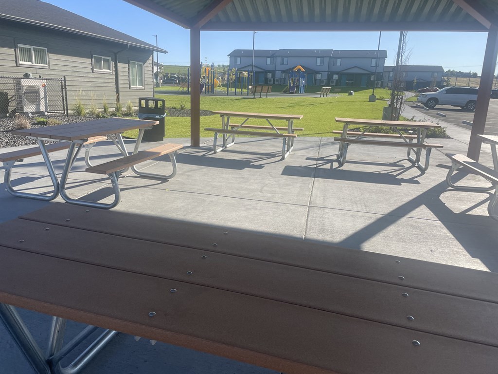a patio with picnic tables and a playground in the background