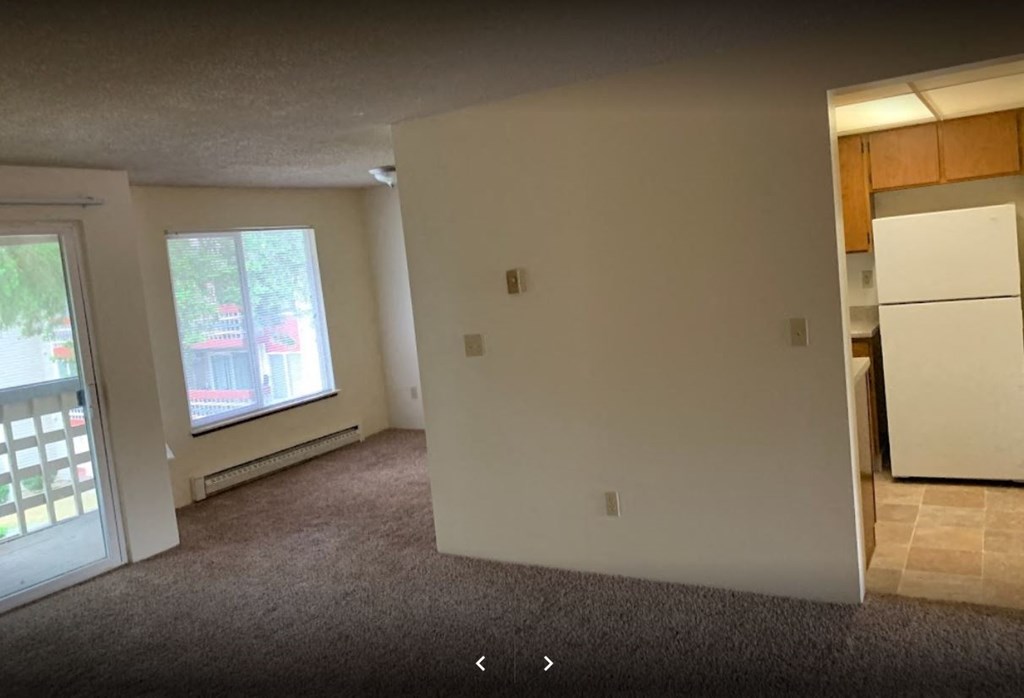 an empty living room with a refrigerator and a window