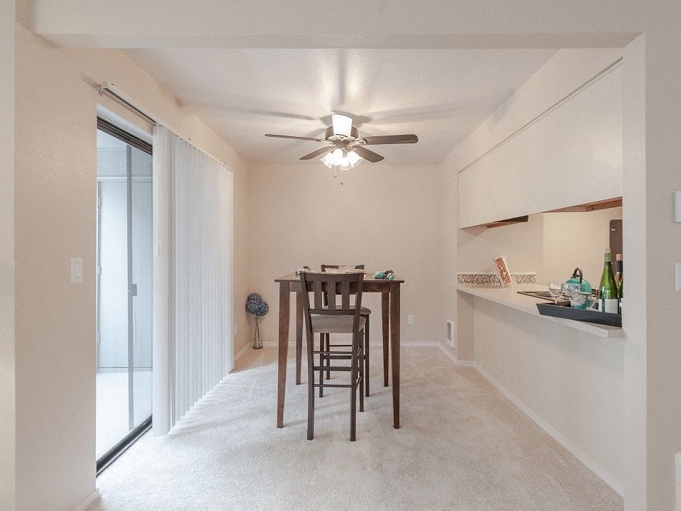 an empty living room with a dining table and a ceiling fan