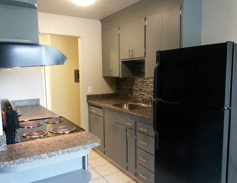 A black refrigerator sits in a kitchen with a granite countertop and stove.